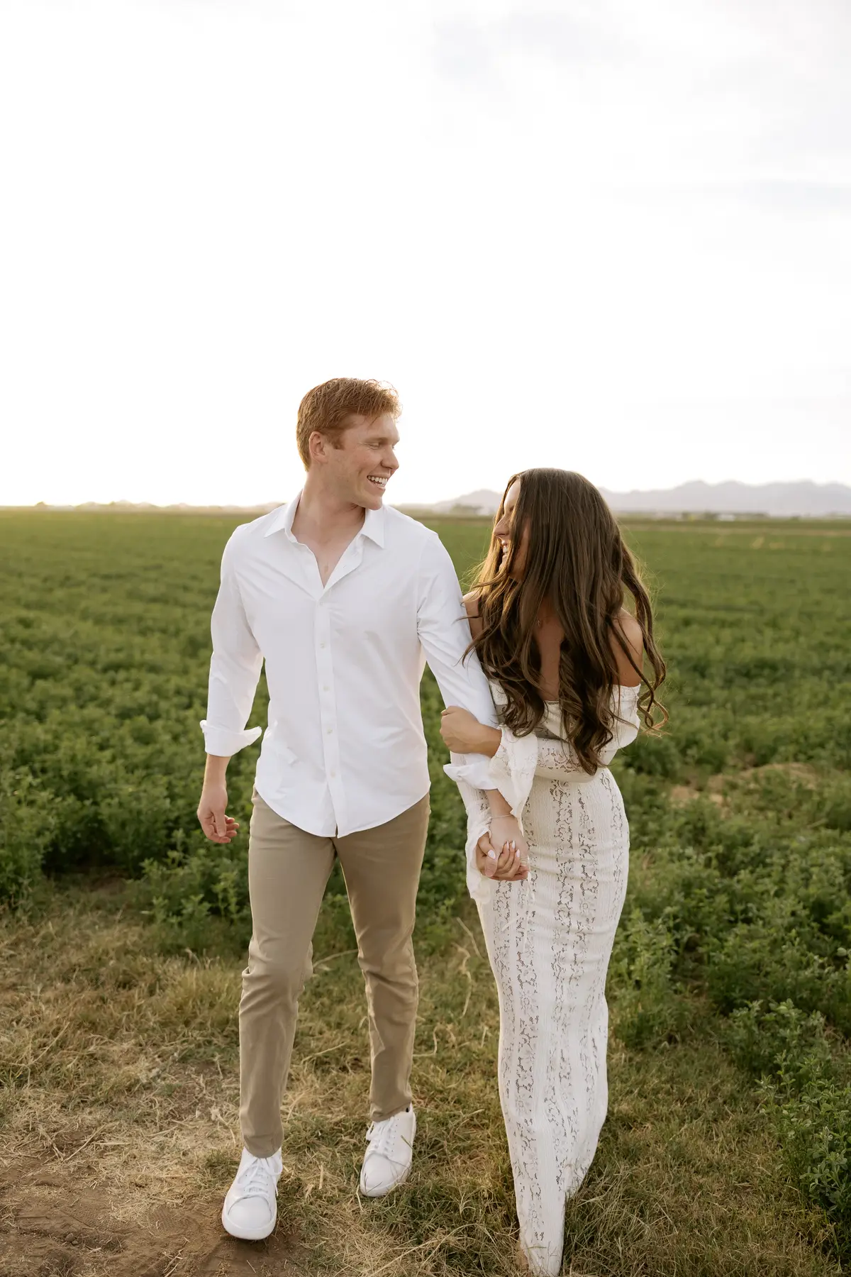 Denae and Kyle walking through an open field at sunset